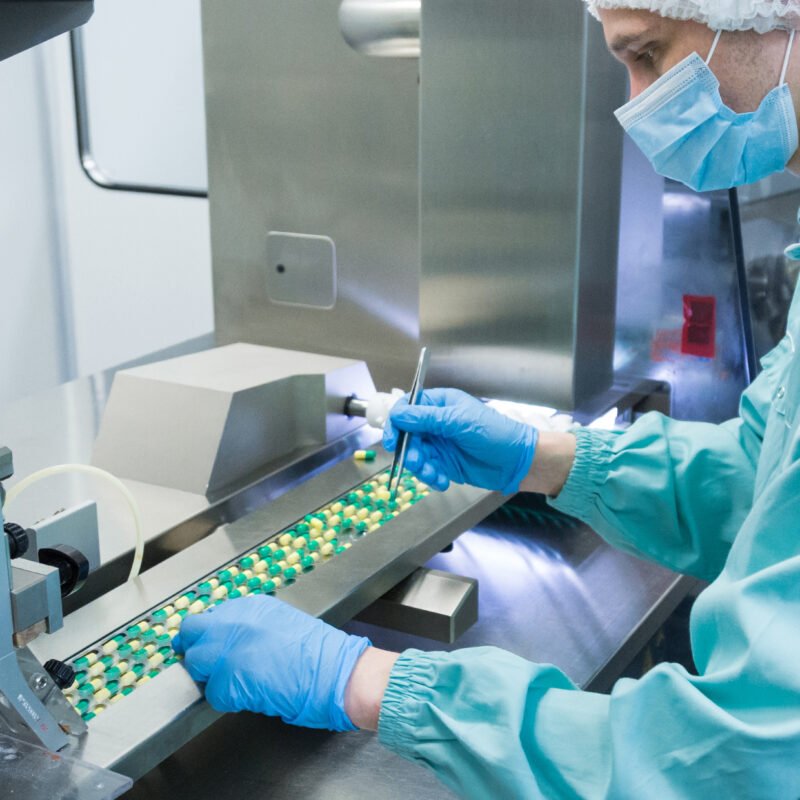 Quality control technician inspecting capsules on a supplement manufacturing production line in a sterile facility.