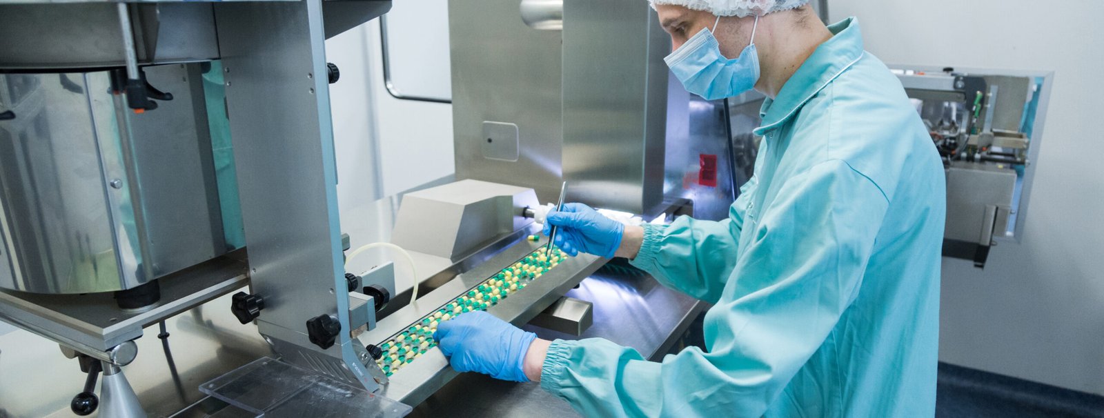 Quality control technician inspecting capsules on a supplement manufacturing production line in a sterile facility.