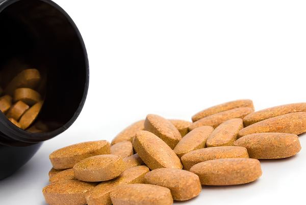 Brown supplement tablets spilling from a black supplement bottle.