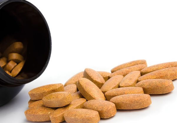 Brown supplement tablets spilling from a black supplement bottle.